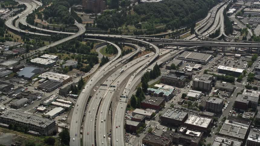 Aerial footage approaches the interchange of Interstate 5 and 90 Express capturing the movement of cars and the urban landscape of Greater Duwamish Seattle