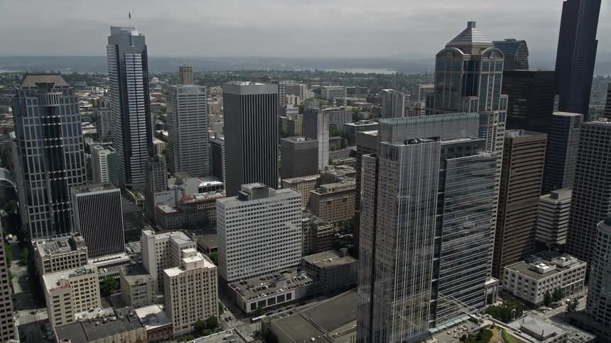 Flying over a cloudy Downtown Seattle to approach the impressive Rainier Tower surrounded by high-rises and skyscrapers