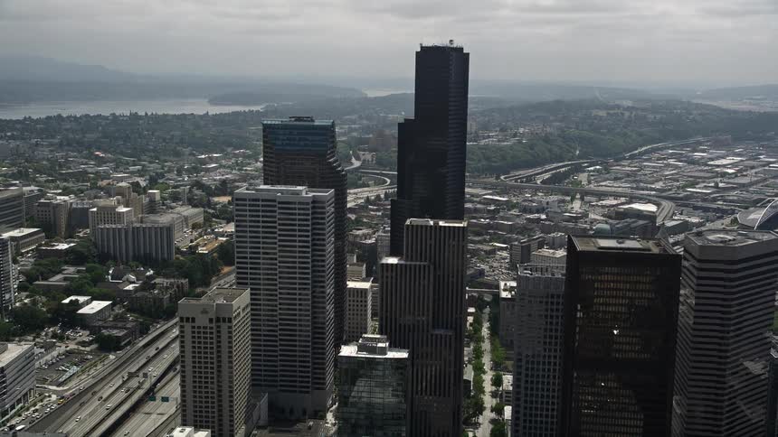 Aerial footage of high-rise buildings and skyscrapers in Downtown Seattle with Columbia Center approaching in partly cloudy skies