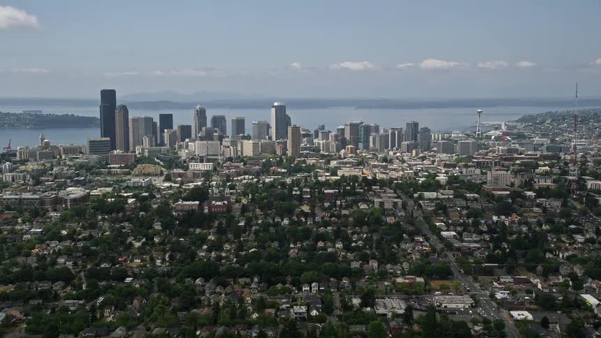 Aerial footage of Downtown Seattles skyline from central neighborhoods on a partly cloudy day with a perspective approaching the citys high rise buildings and towers