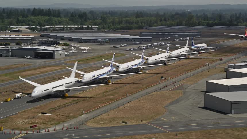 Six commercial airliners lined up on the tarmac at Paine Field with smaller planes in the distance