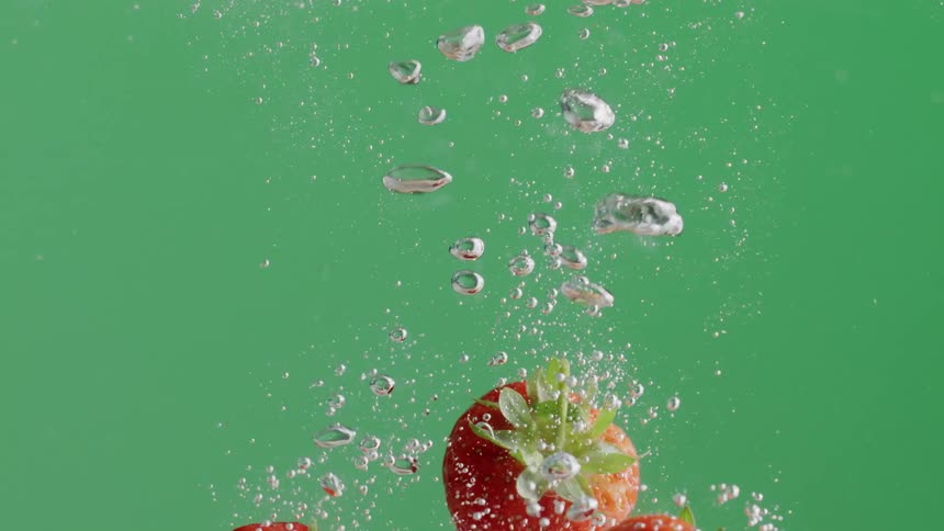 Three strawberries falling into and then floating in water in front of a green background