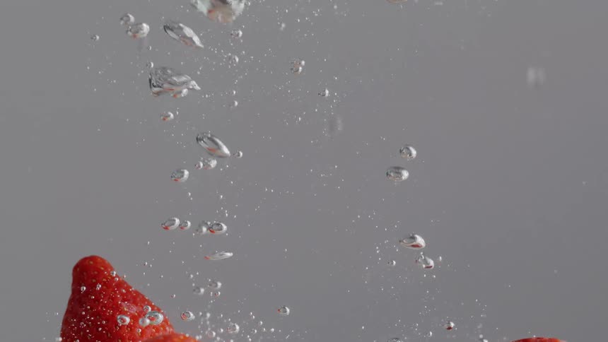 Three strawberries are dropped into and then float in water in front of a purple background