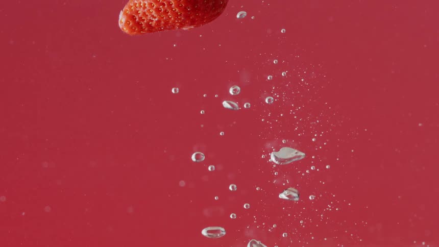 A strawberry flies upward in a container filled with water as air bubbles float up and down