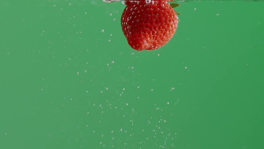 A strawberry falls into and then floats in water in front of a green background