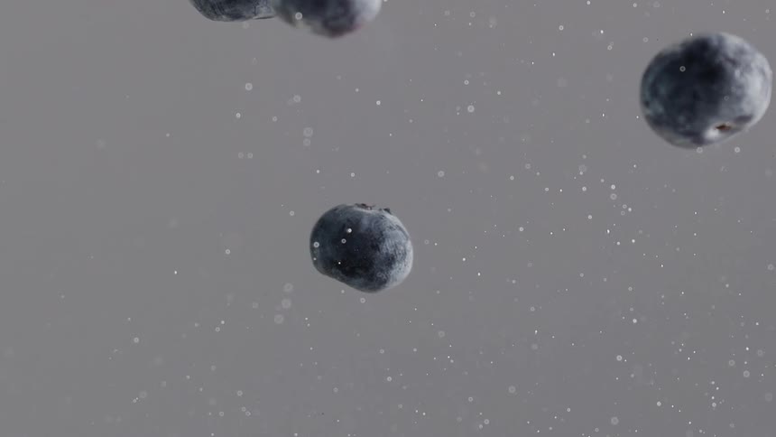 Blueberries float among bubbles against a gray background