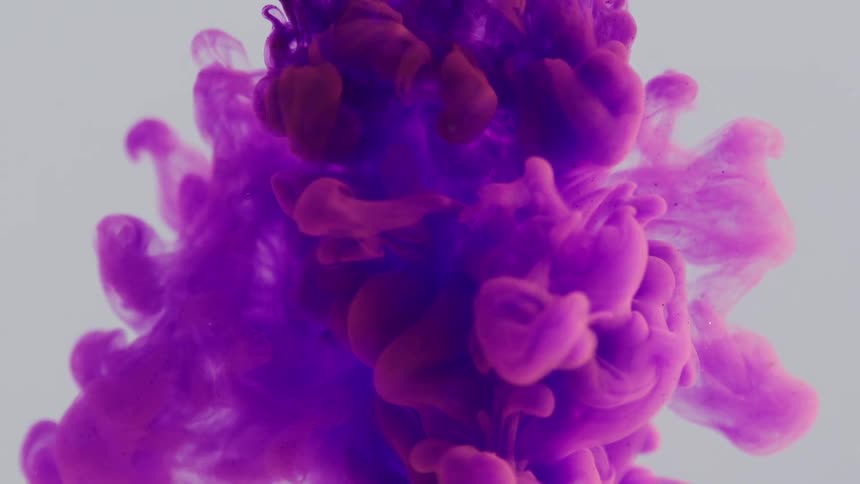 Purple liquid being poured into and flowing in transparent liquid