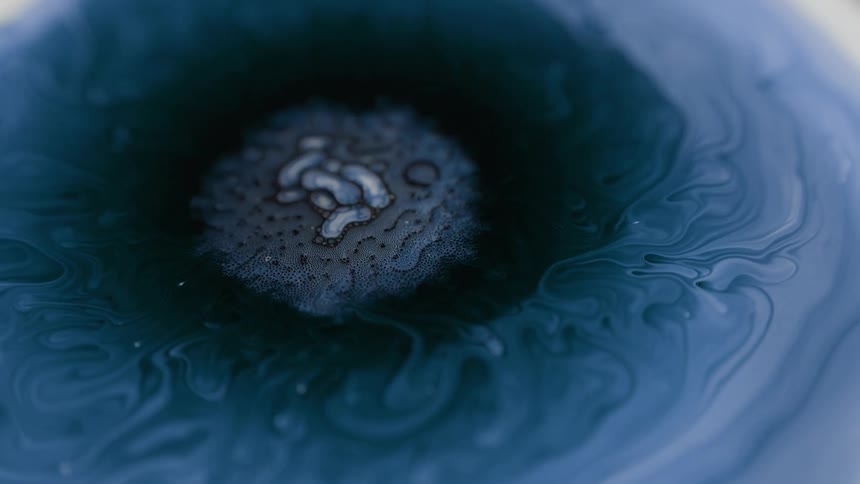 Blue swirls around a dark liquid substance as an organic amoeba rises to the surface and spreads