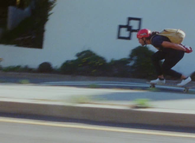 A teenage boy is wearing a backpack and riding a skateboard as he bends down while coasting on a neighborhood street