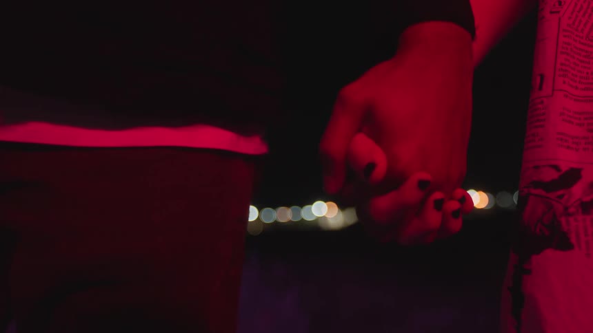 Couple hold hands at night with city lights in the distance