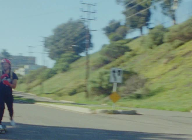 A skateboarder using his foot to gain speed as he goes downhill on a road