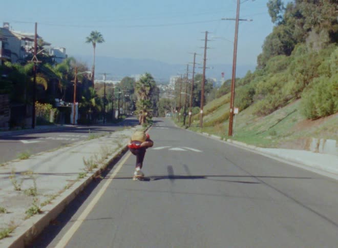 Skateboarder with brown backpack and red gloves skateboards down highway