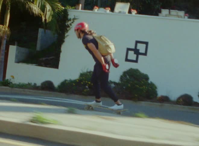 Man skateboards down road bordered by walls and fences