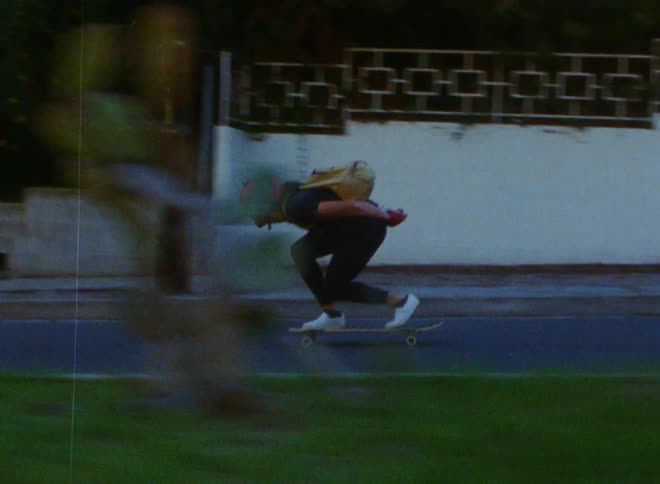 Man with red helmet black t shirt pants and white shoes skateboards downhill in the street