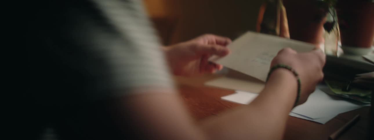 Person walks into room and sits at desk before opening envelope