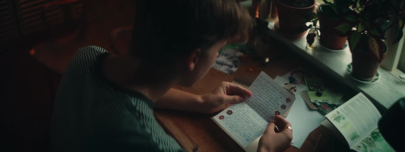 A young male sits at a desk and unfolds a note that he begins to read