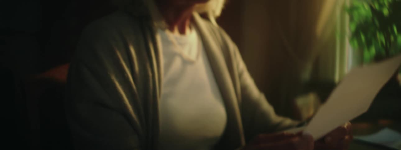 Happy grandma sitting at desk with the sun pouring in from the window reading a handwritten letter and smiling