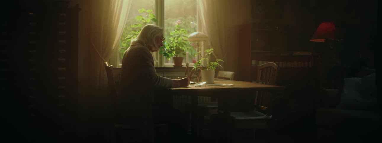 A woman writes while sitting at her dining room table in front of a window