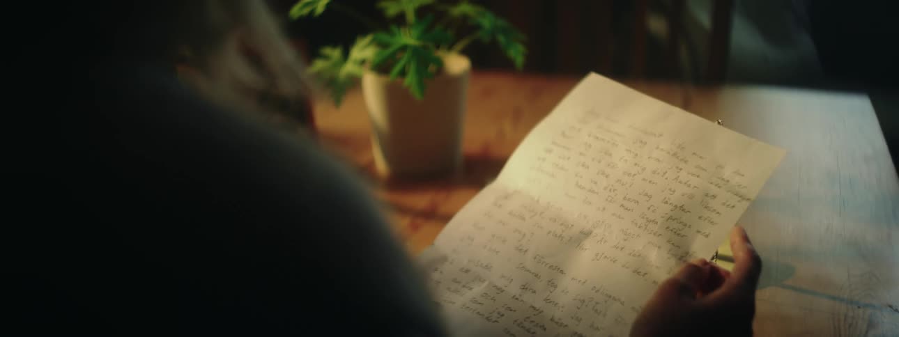 Woman sitting at table near window smiles while reading a handwritten letter