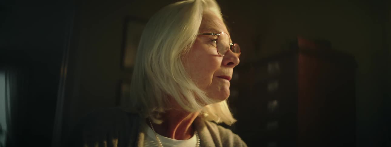 A white haired woman sits at a table while writing a note on a piece of paper