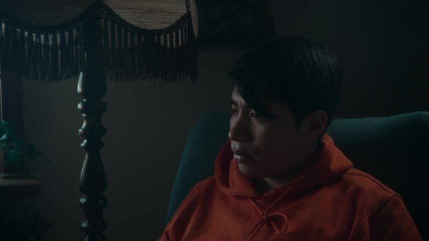 Man in orange hoodie sits in armchair next to windows and floor lamp