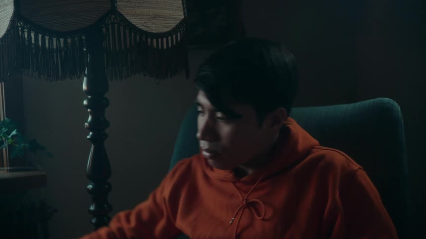 Teenage boy sitting on easy chair in living room leans forward to grab game controller and sits back and watches tv