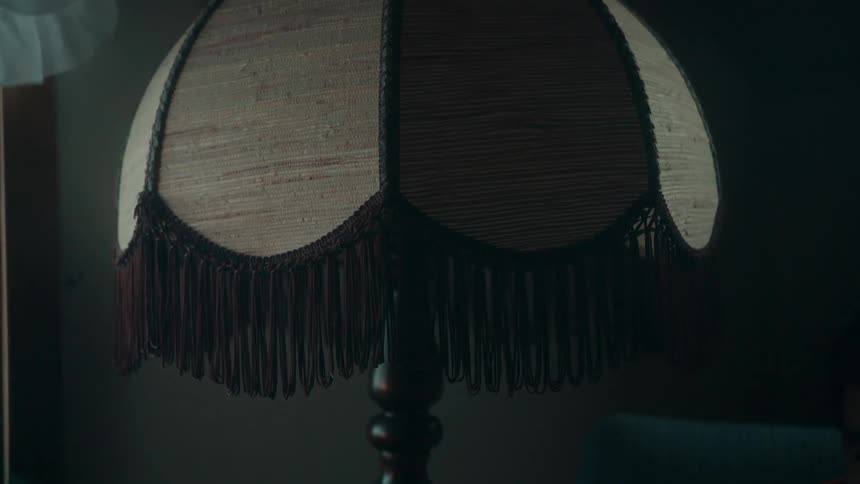 A tan lamp shade with brown tassels hanging down as the light turns on and off
