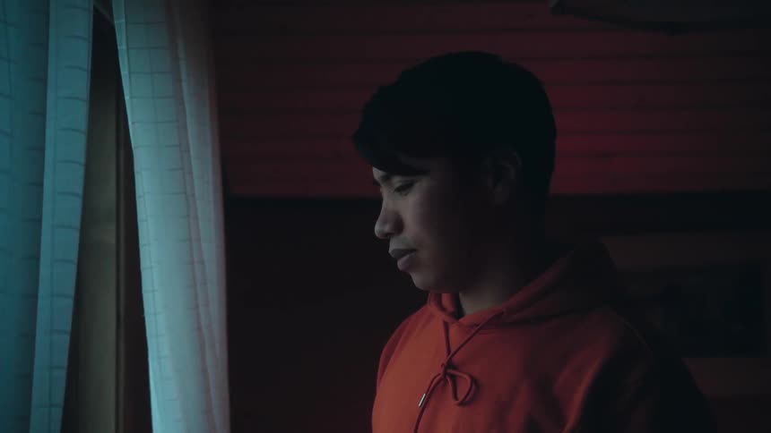 Young man standing on a room looking out of a window