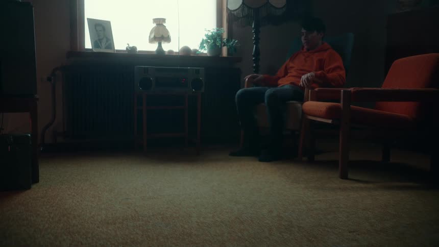 A close up of a rug revealing a teenage boy sitting in a chair next to an old radio