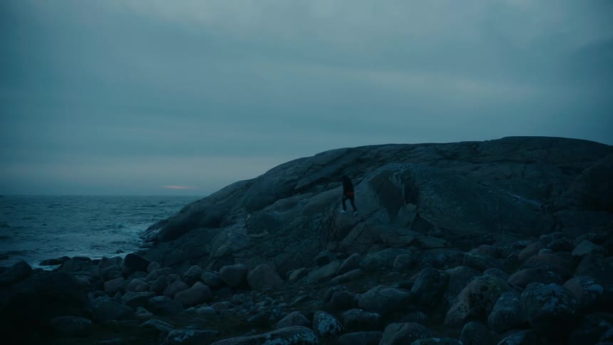 A man walks over the rocks on the shore