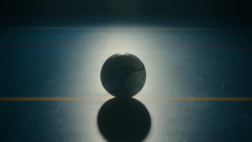Close up of a volleyball standing on the floor of an indoors court projecting a shadow
