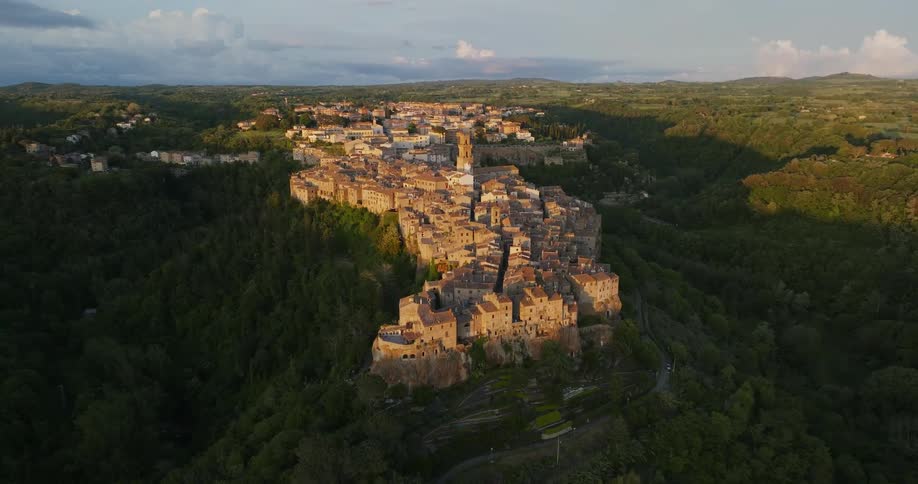 Shadows fill valley near crowded old world town sitting on hill among forest