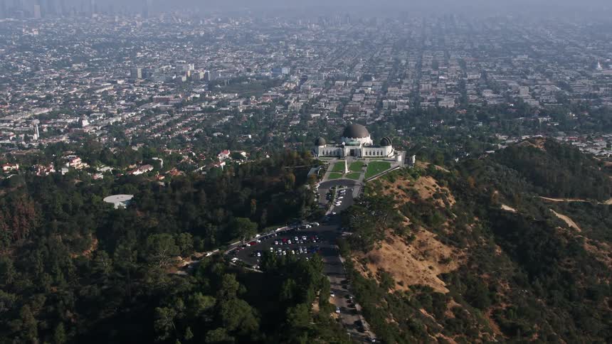A breathtaking 4K aerial view of the Griffith Observatory and Hollywood Hills overlooking the hazy city of Los Angeles on a beautiful day