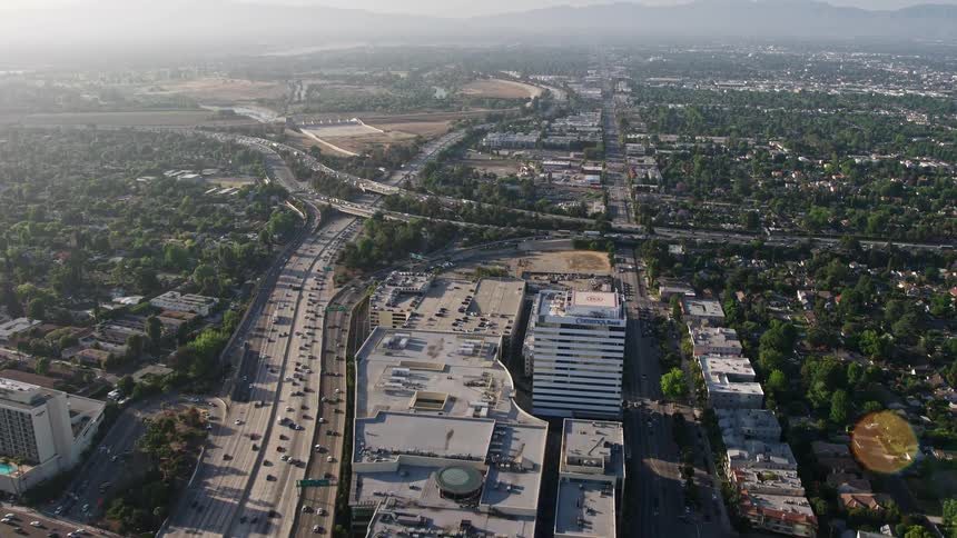 Aerial footage of heavy traffic approaching the I-405 and 101 interchange passing over office buildings and the Sherman Oaks Galleria in California