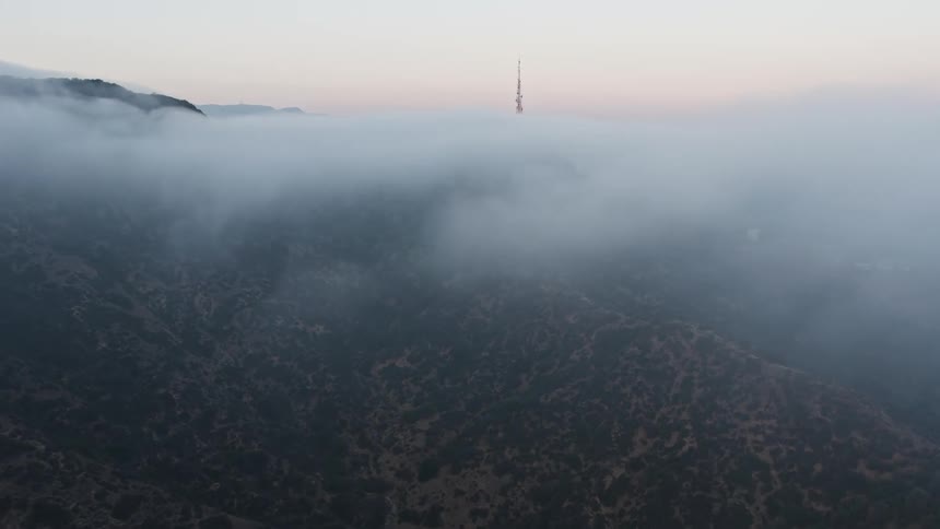 Approaching iconic radio tower through marine layer revealing Hollywood Sign during a beautiful California sunset