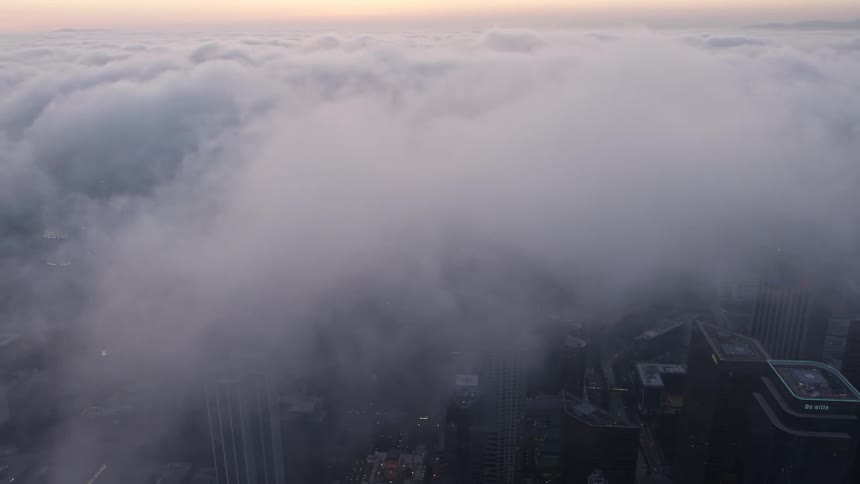 A stunning sunset aerial view of downtown Los Angeles covered in a marine layer with towering skyscrapers disappearing into the clouds