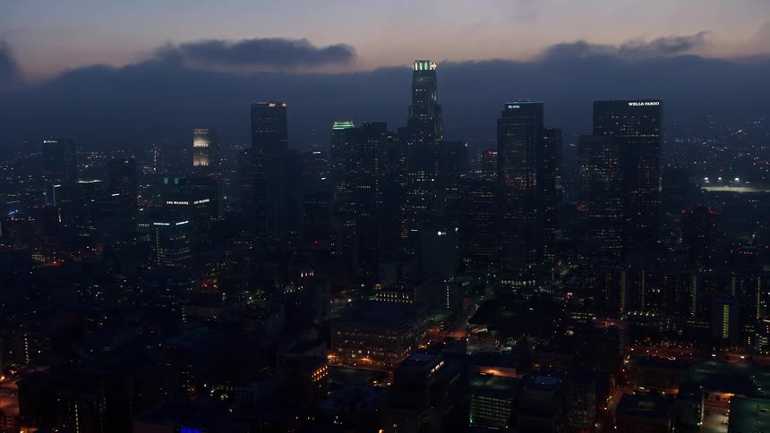 Aerial footage flying over Downtown Los Angeles at twilight showcasing a stunning cityscape below a marine layer