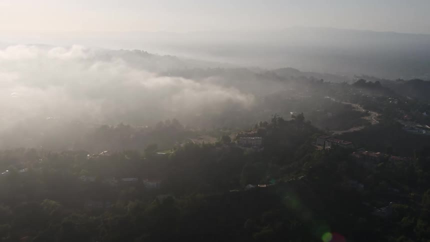 A 4K aerial video approaches upscale hillside homes in Beverly Hills California with a marine layer rolling over them