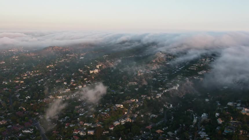 Aerial footage of a foggy evening descends over tall hillside houses with a colorful sunset in the background in Sherman Oaks California