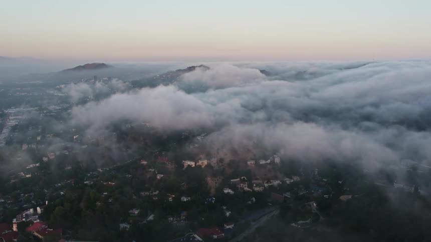 Flying over homes in Studio City California during sunset capturing the marine layer flowing over hills