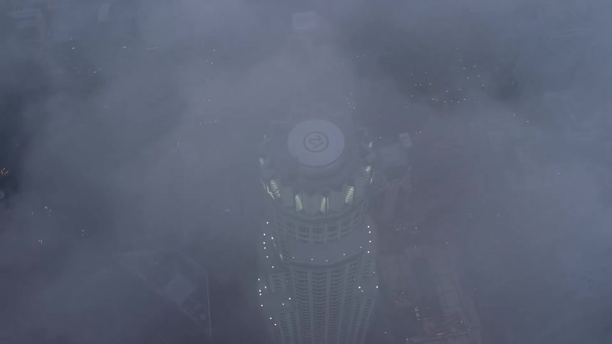 A breathtaking 4K aerial view of US Bank Tower at twilight shot from a birds eye view through the marine layer as it overlooks the bustling downtown Los Angeles with clouds obscuring the view from above