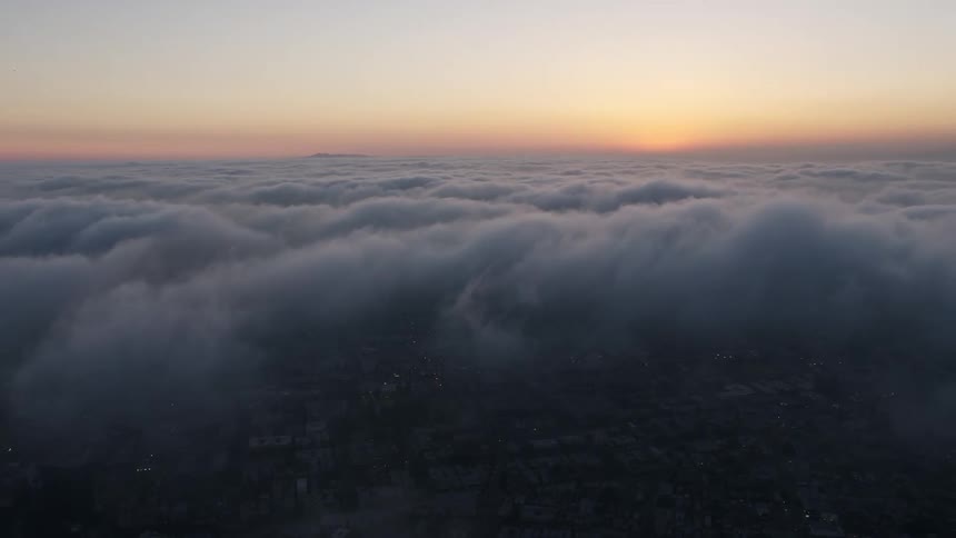 Aerial footage panning right over thick marine layer at sunset with dark clouds forming over Hollywood California