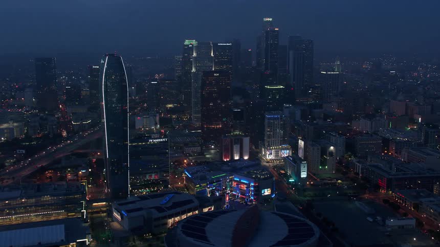 Approaching towering high-rises and skyscrapers captured in stunning 4K aerial footage as the city transitions into a beautiful twilight in Downtown Los Angeles