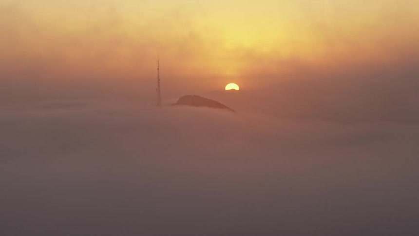 Aerial view of the sunset behind Hollywood Hills with a radio tower covered in marine layer visible in the footage