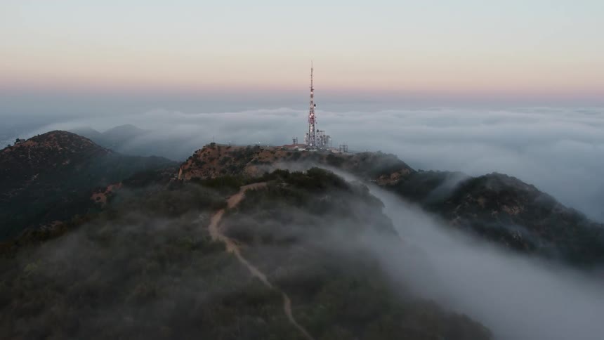 Aerial footage of Marine Layer rolling over Hollywood Hills during sunset in Los Angeles revealing radio towers and scientific facilities with a tilt up shot
