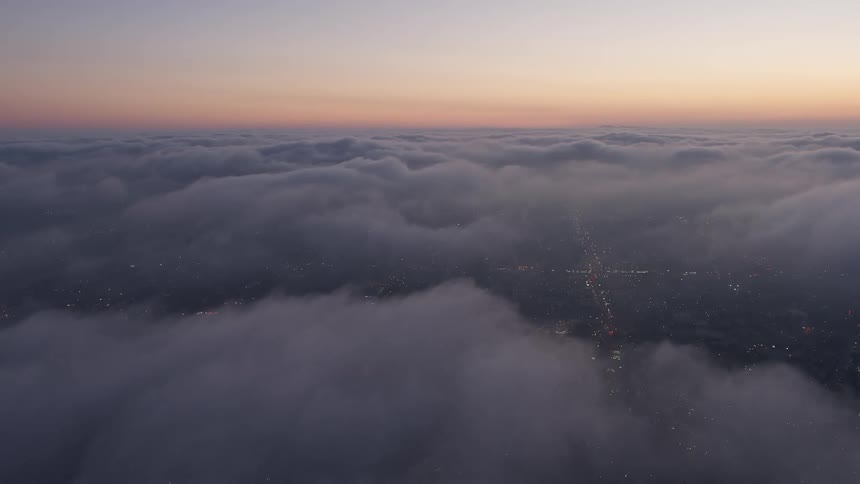 Aerial footage of Los Angeles during twilight showing a marine layer with the city coming to life as day dawns below
