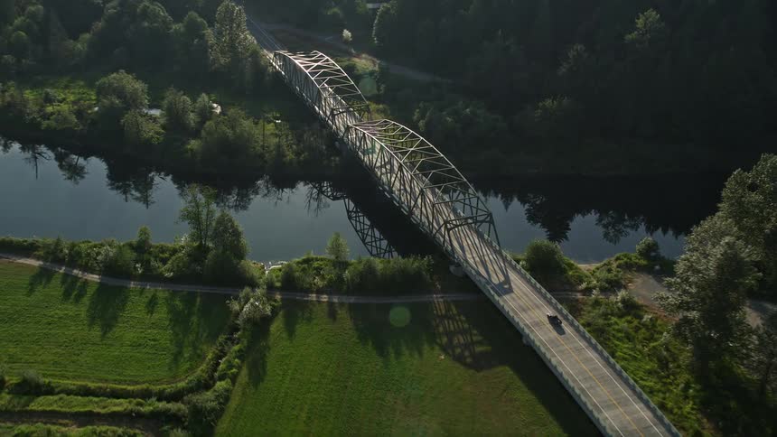 Aerial footage tracking a truck as it crosses a bridge over the Snoqualmie River in Carnation Washington on a sunny day