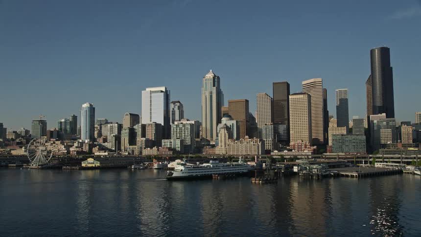 Aerial footage of the Downtown Seattle skyline and Central Waterfront with a motor boat leaving a wake as it heads towards the dock on the edge of downtown