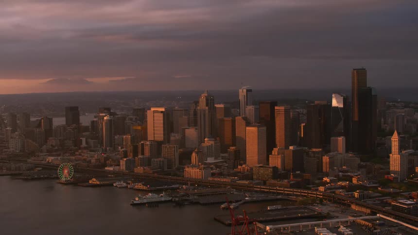 Skyscrapers loom over the coast of a metropolis at sunset on a cloudy evening