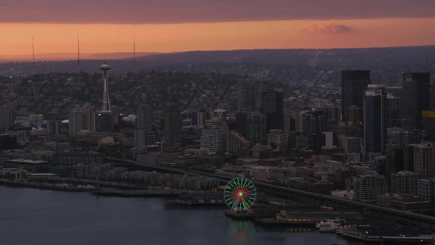 Aerial view of high rise buildings and illuminated ferris wheel near the sea at sunset